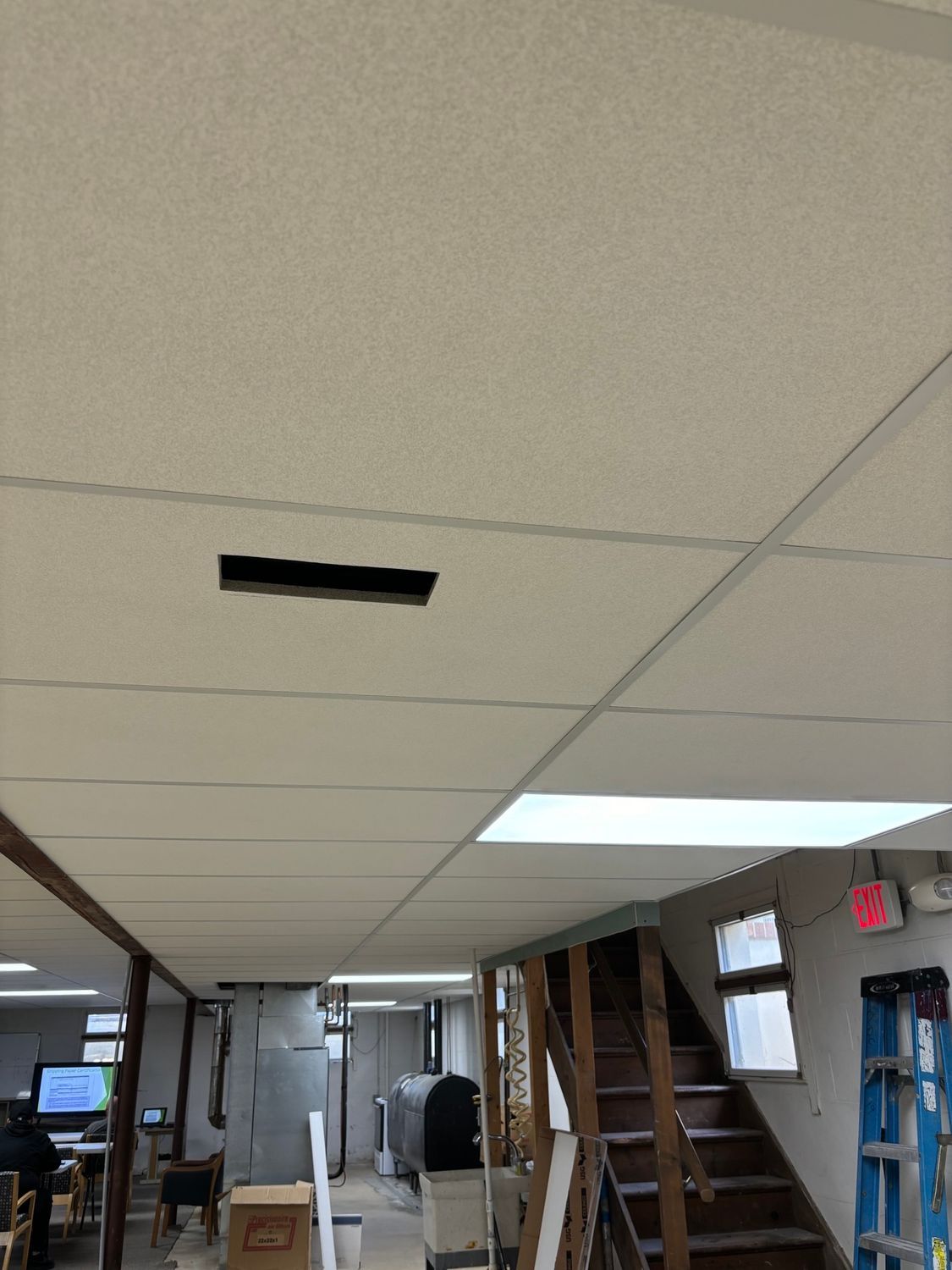 Ceiling with a rectangular hole and drop ceiling tiles. Staircase and room with construction.