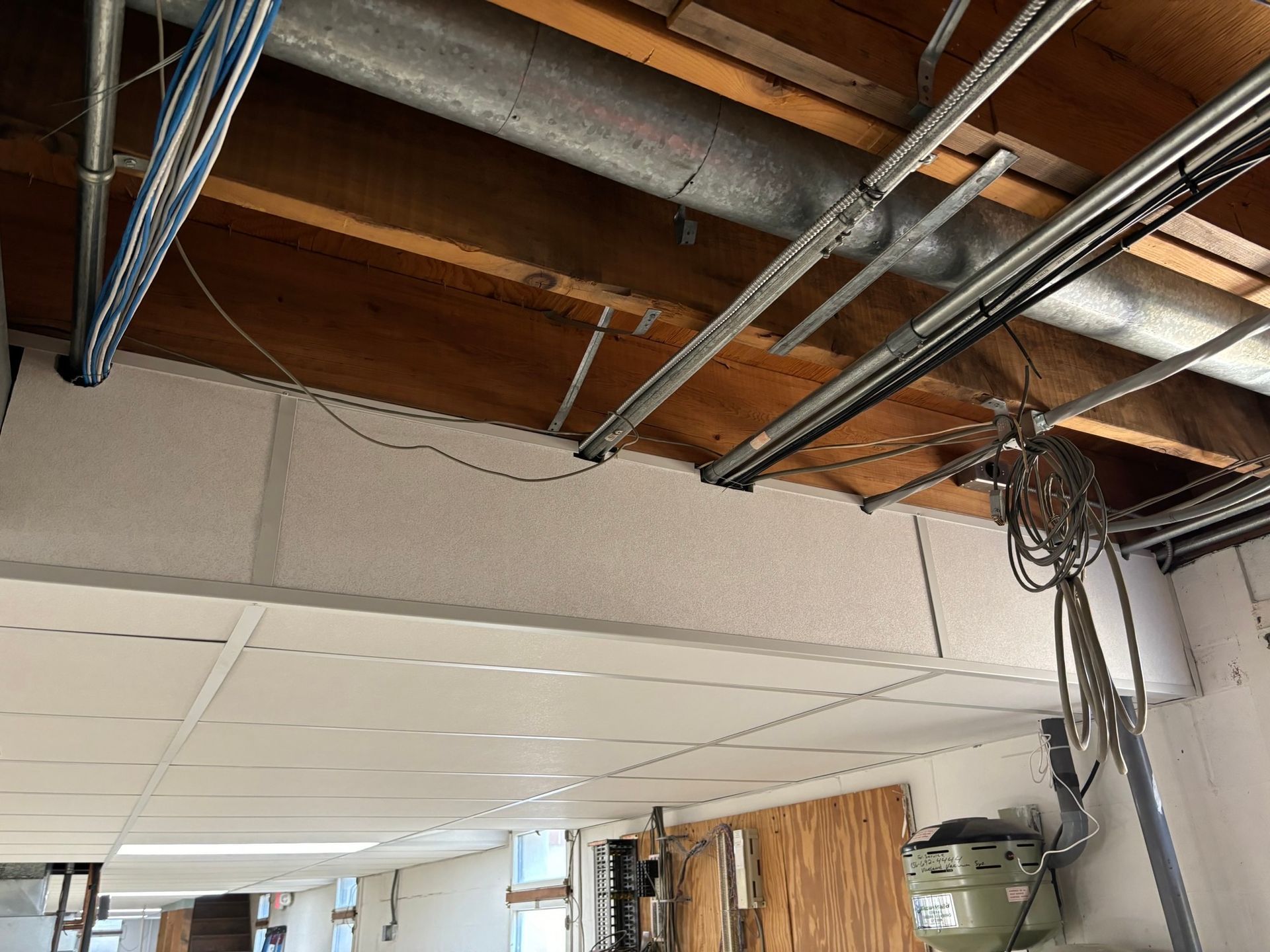Ceiling with exposed wiring, pipes, and ceiling tiles.