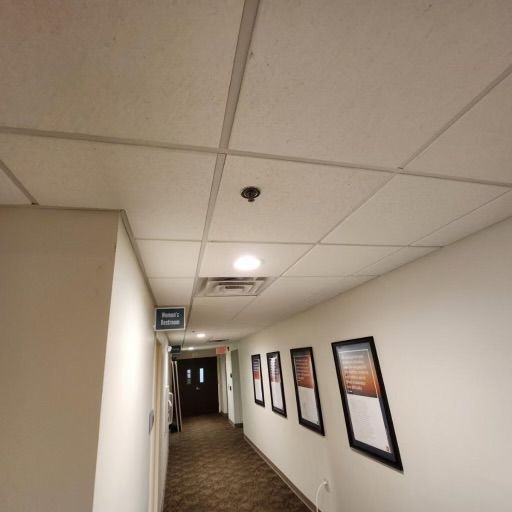 Hallway with white walls, framed artwork, and a drop ceiling.