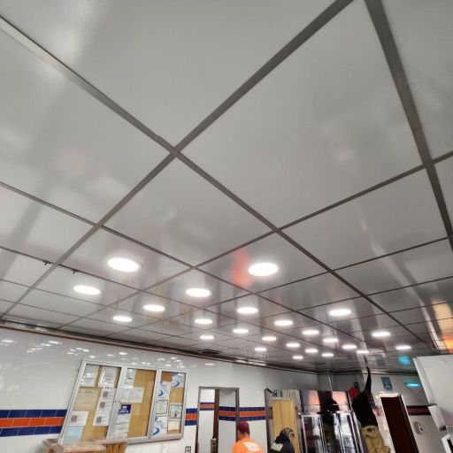 White ceiling with grid and recessed lights. People standing in a room with a bulletin board.