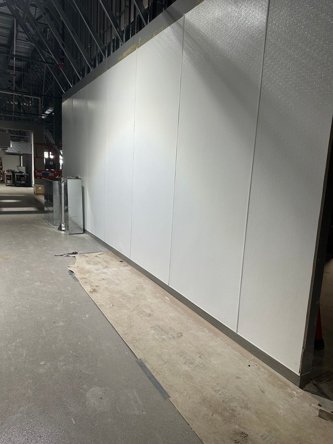 White insulated panels forming a rectangular structure in a warehouse. Gray flooring and exposed ceiling beams.