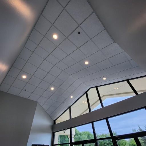 Low-angle shot of a white tiled ceiling with recessed lights, above tall windows.