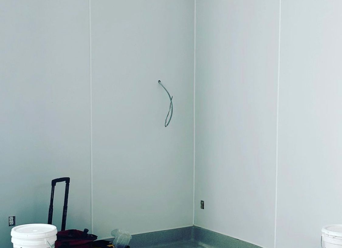 Interior corner of a room with white walls, a wire, and a bucket.