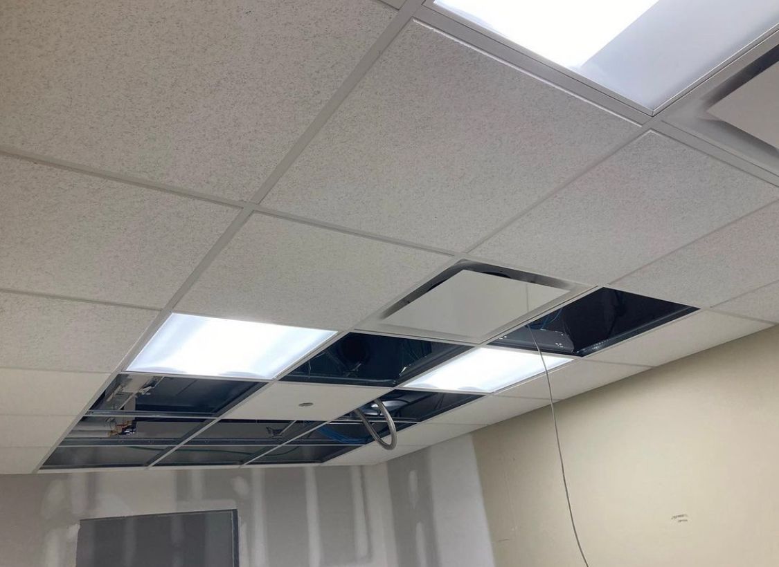Ceiling tiles removed, revealing exposed metal grid, lights, and wiring in a room.