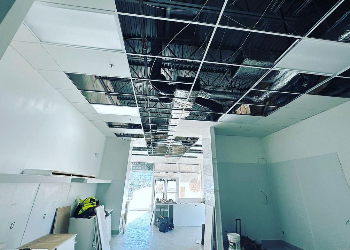 Construction site interior with exposed ceiling grid, reflective insulation, and drywall.