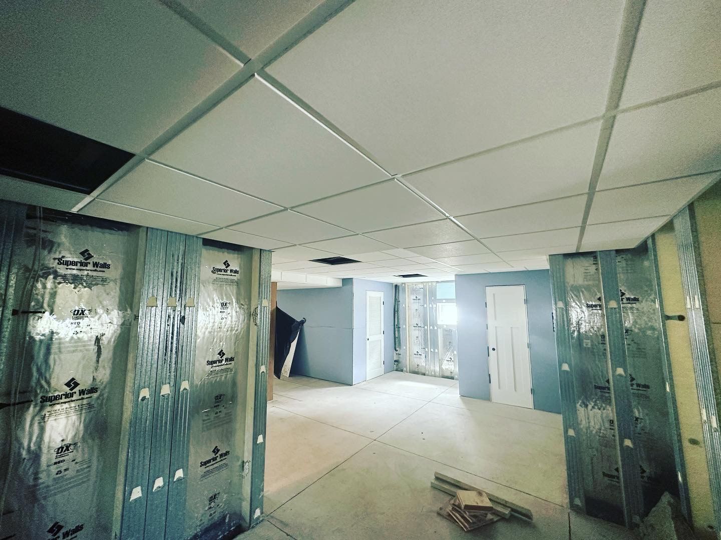 Construction site interior with drop ceiling and exposed metal framing. Walls have insulation and a doorway.