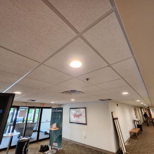 Acoustic ceiling tiles with recessed lighting in a room with a white wall, a welcome sign, and a framed 
