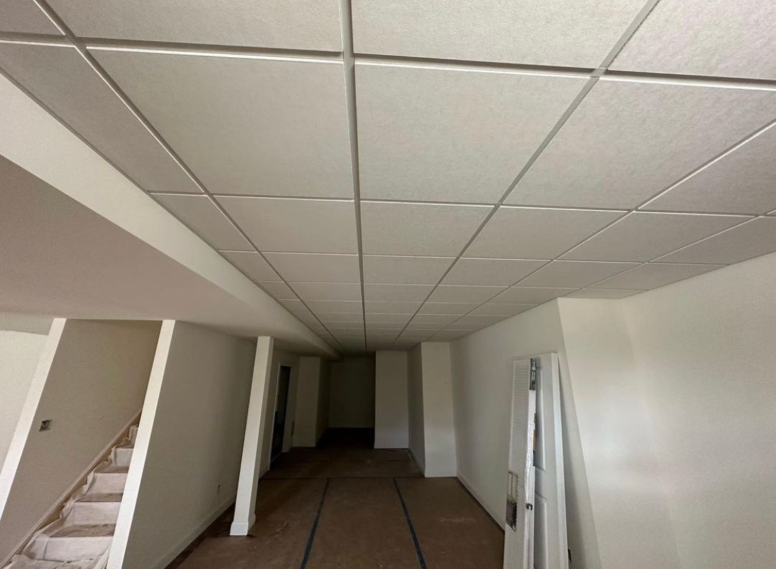 An interior view of a room with a suspended ceiling, white walls, and a wooden floor.
