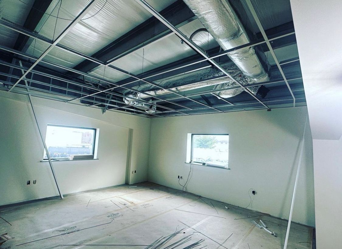 Interior room under construction with exposed ceiling framework, ducts, and windows.