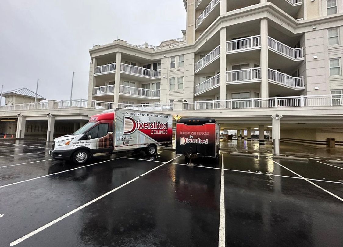 Two service vans parked in front of a multistory building with balconies on a wet, paved parking area.