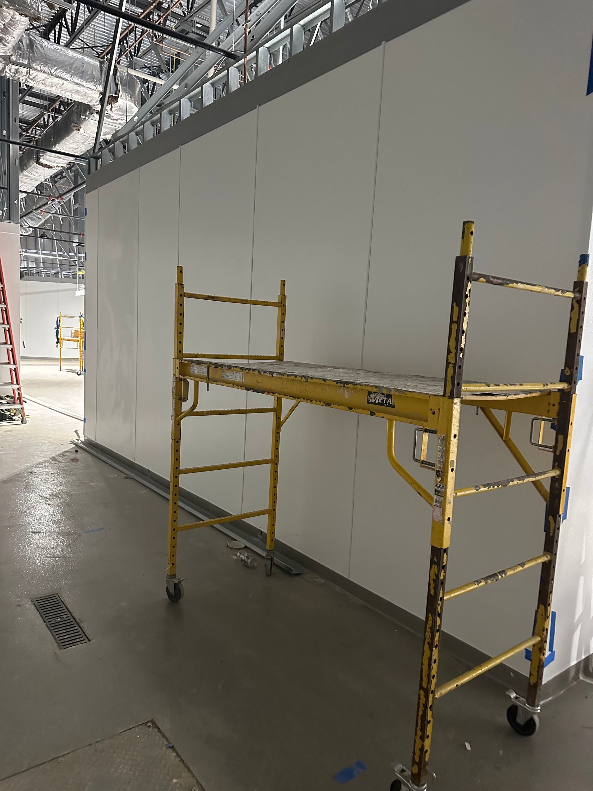 A yellow scaffolding sits in front of a white wall in an unfinished building.