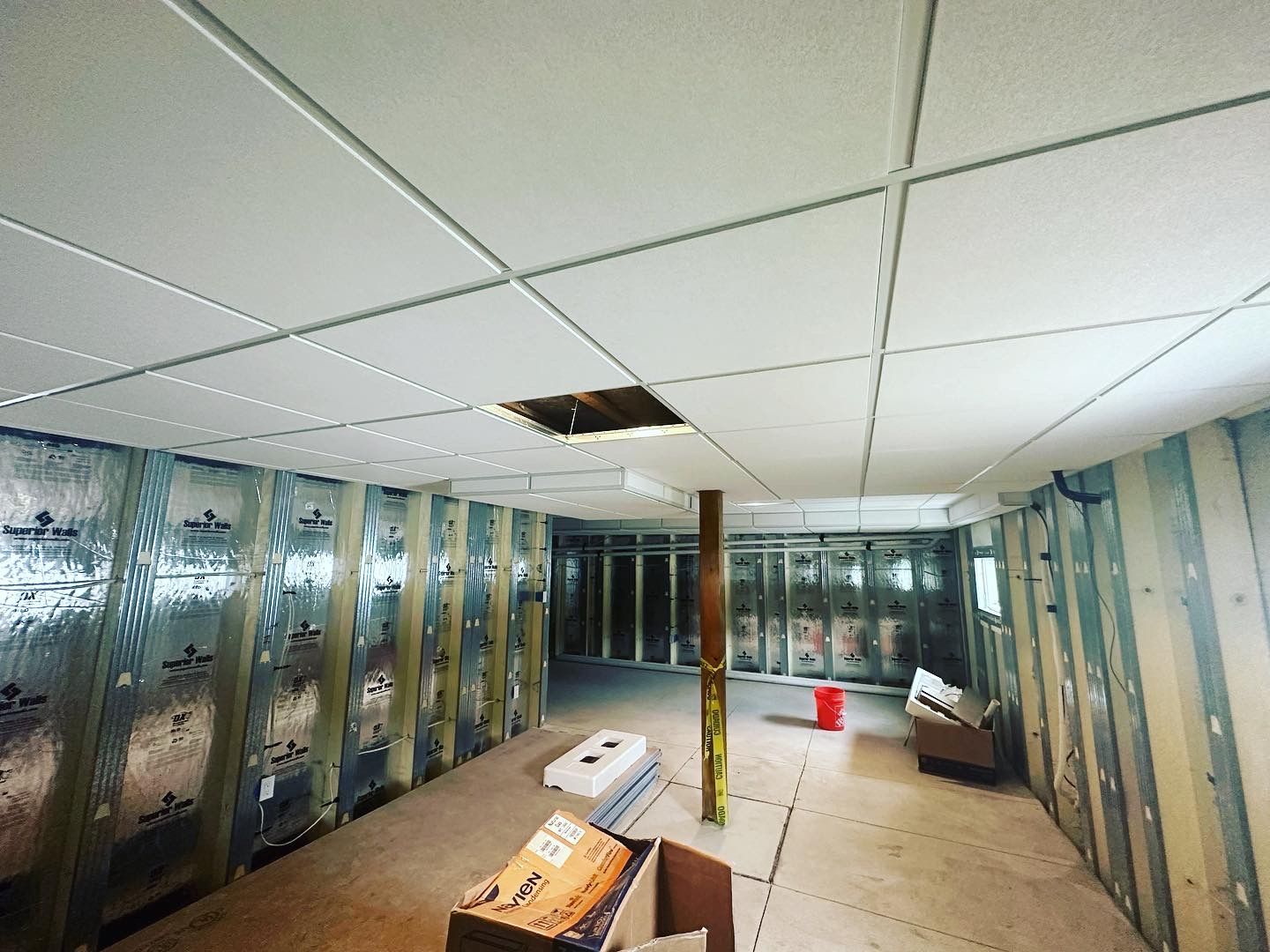 Interior of a room under construction with a drop ceiling, insulated walls, and unfinished floor.