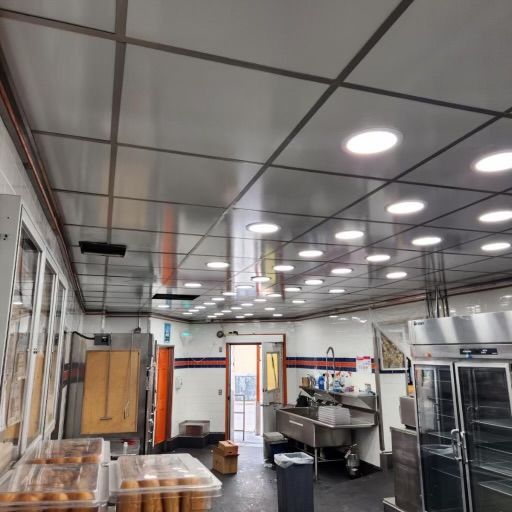 Commercial kitchen interior with stainless steel ceiling, bright lighting, and various equipment.