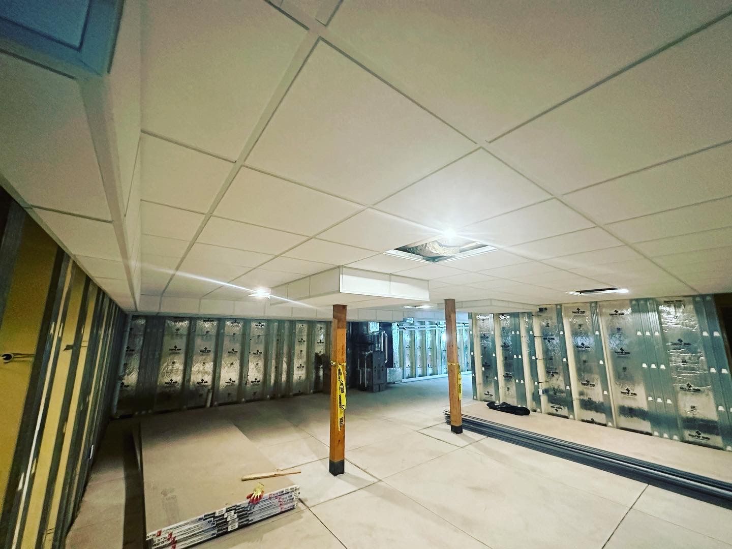 Interior view of a construction site with exposed walls, a grid ceiling, and wood support beams.