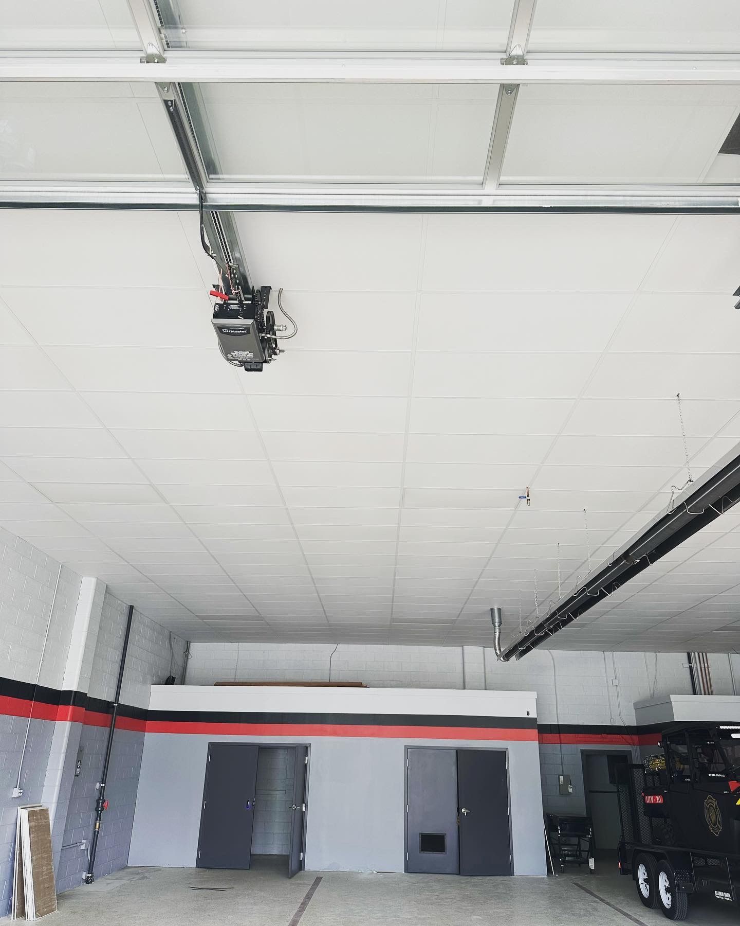Garage interior with a ceiling-mounted garage door opener and closed doors. Gray, red, and black color scheme.