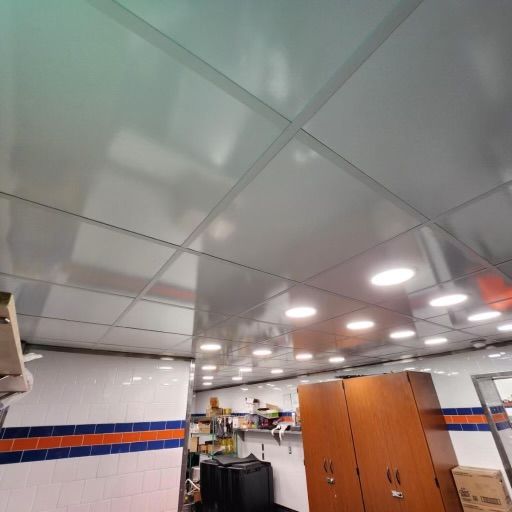 A kitchen ceiling with square panels and recessed lights, white and blue tiled walls, and wood cabinets.