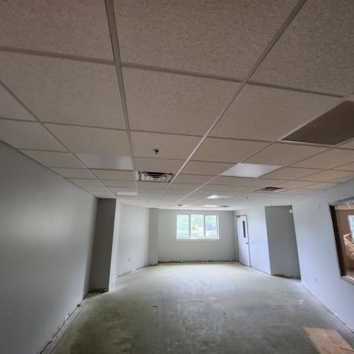 Empty room with drop ceiling, gray walls, and concrete floor. Windows and a door are visible.