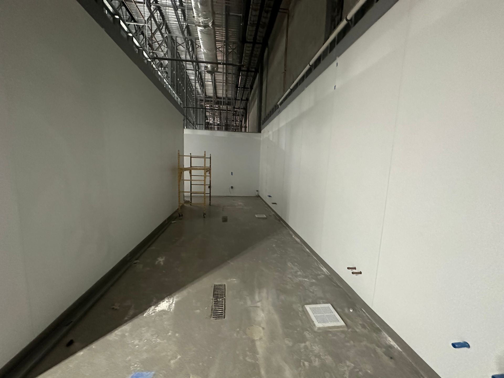 Empty room with white walls and exposed ceiling infrastructure; unfinished construction site.