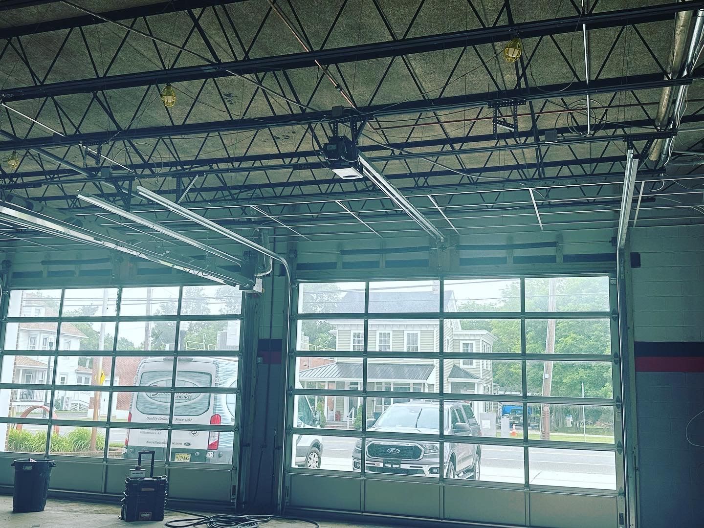 Garage with large glass doors open, cars and houses visible outside.