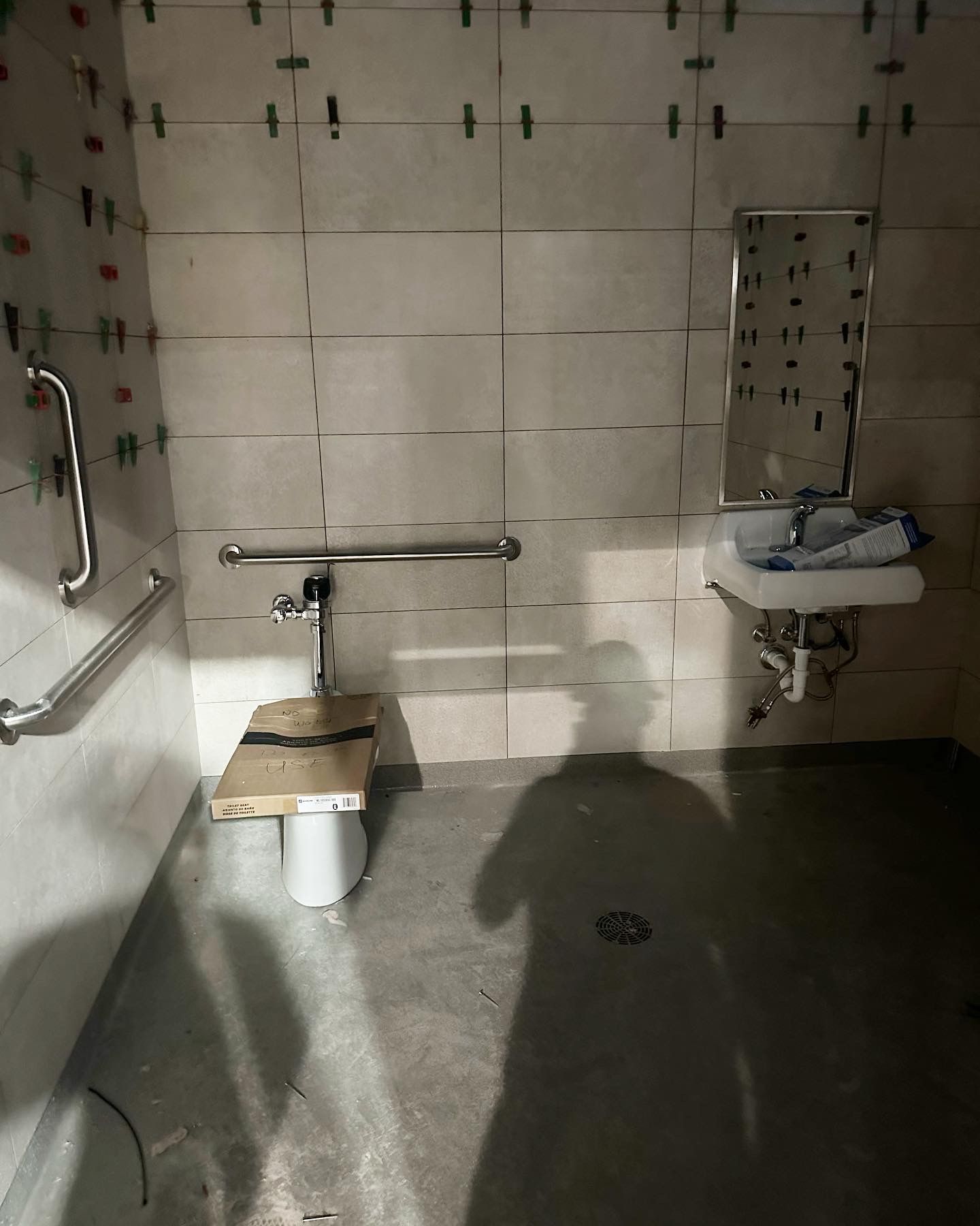 Accessible bathroom under construction with tiled walls, grab bars, toilet, and sink.