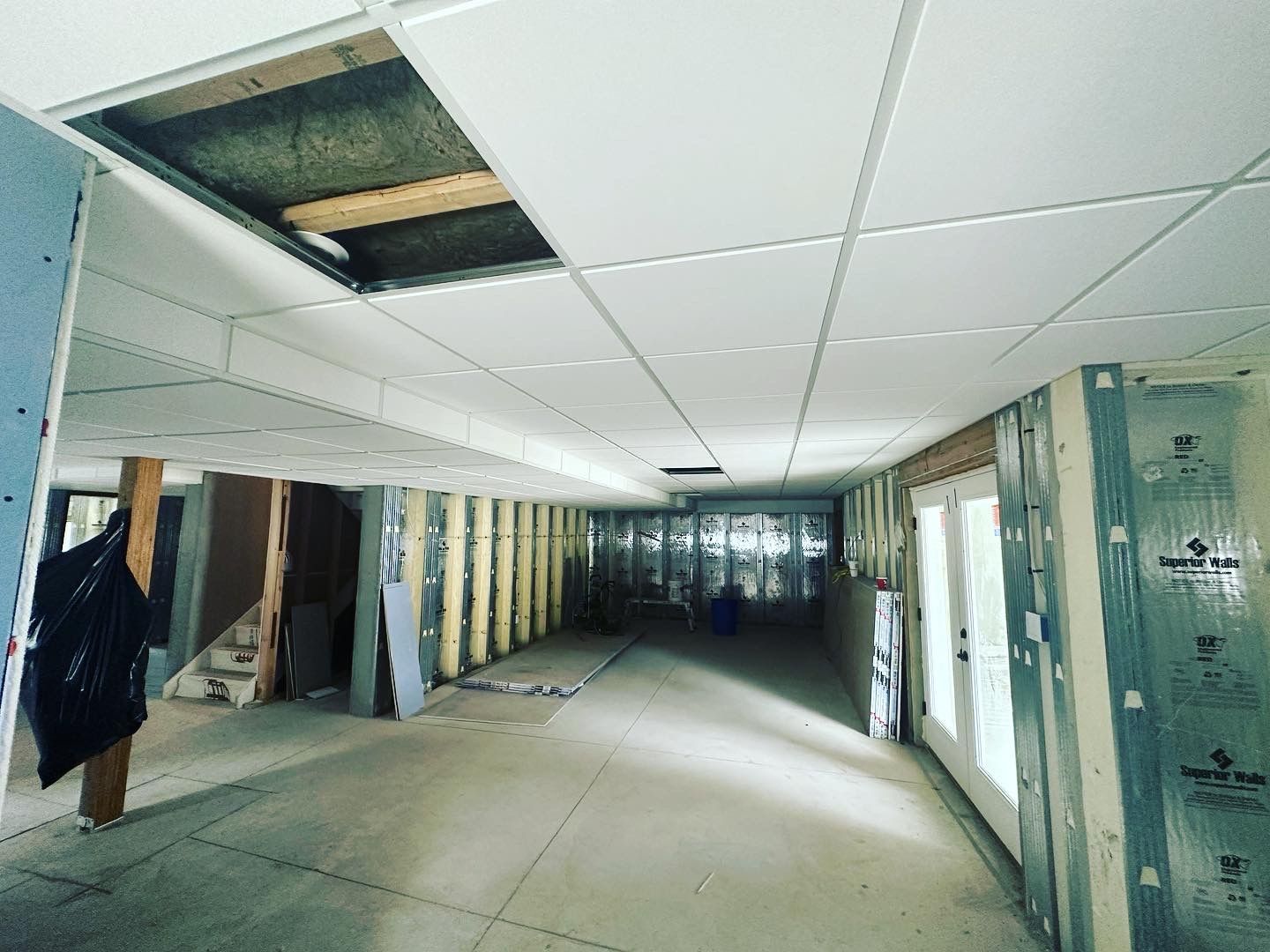 Unfinished interior basement with dropped ceiling, exposed framing, drywall, and double doors.