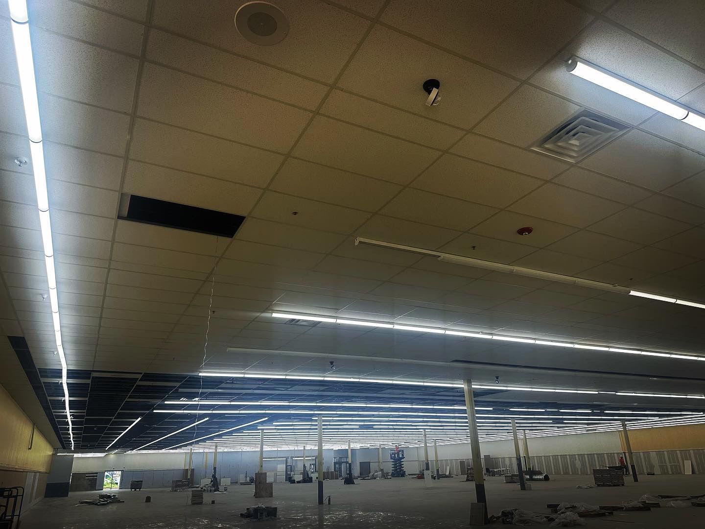 Interior view of a large, empty retail space with a grid ceiling, fluorescent lights, and support columns.