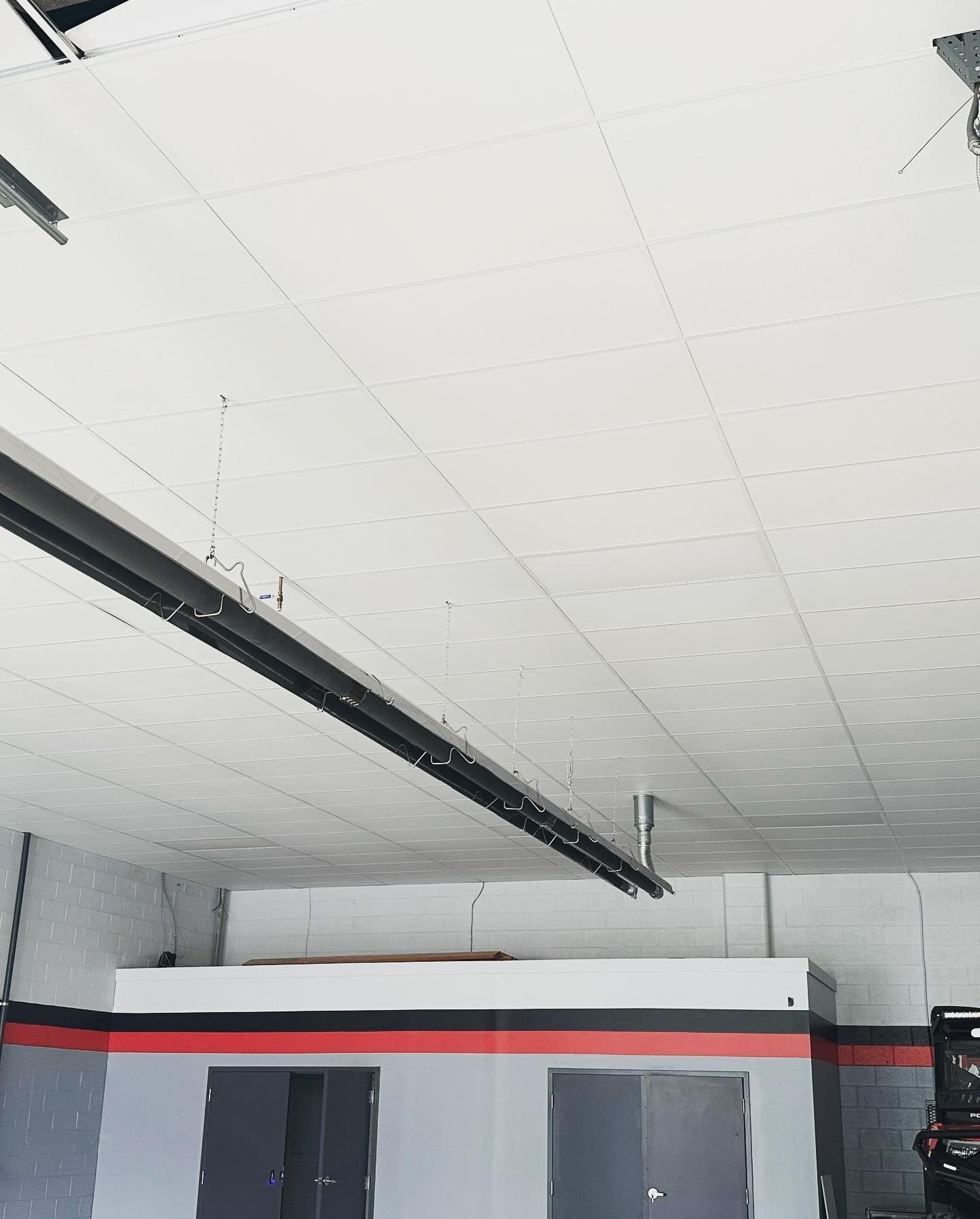 Garage interior with a white ceiling and overhead lights. Walls are gray with red and black accents.