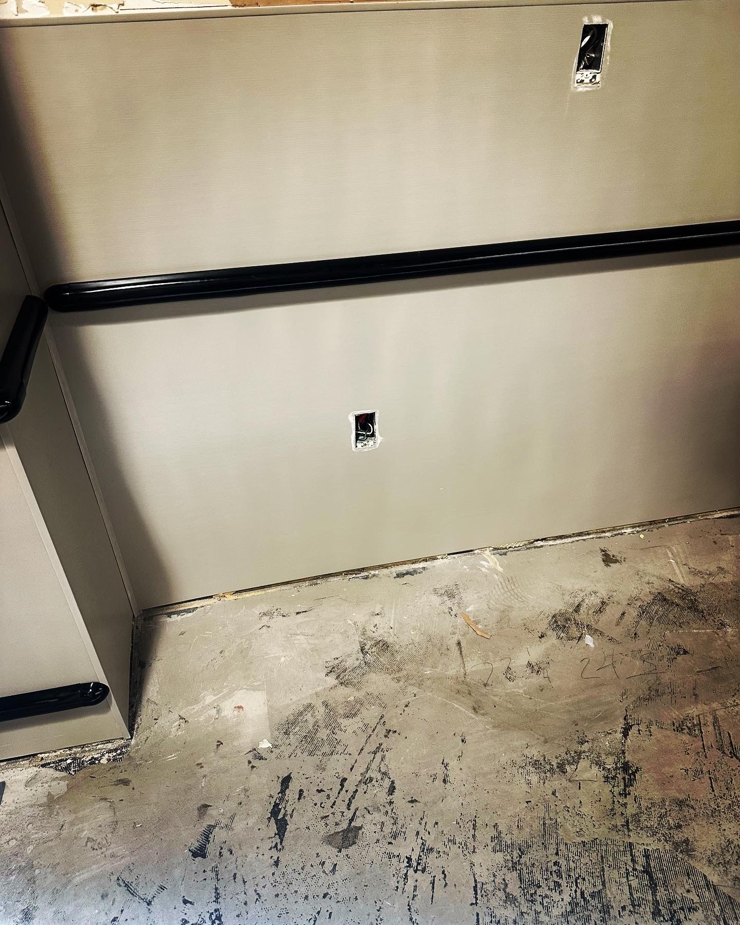 Gray wall with electrical outlets, black conduit, and unfinished concrete floor.