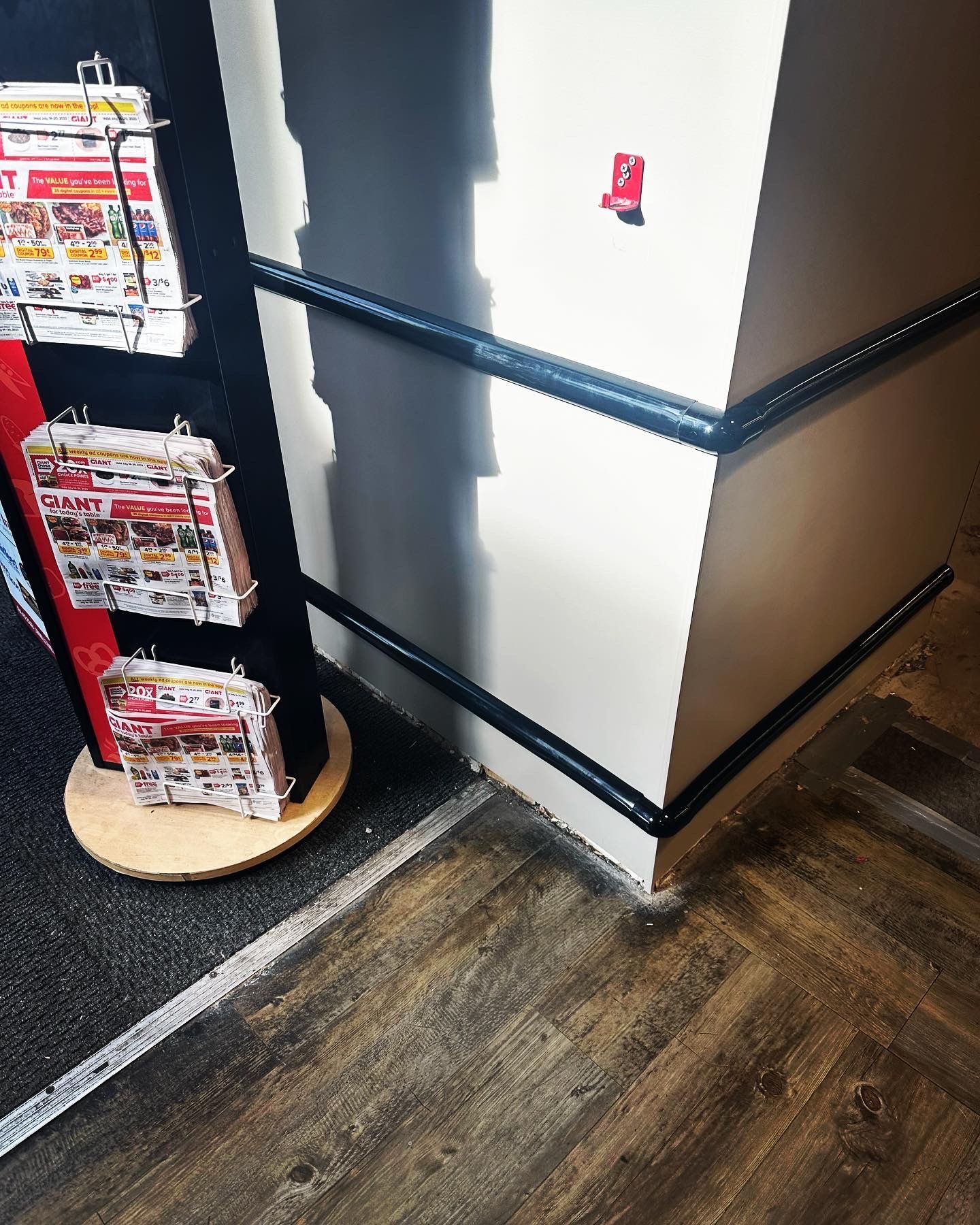 Brochure display stand and wall with black trim, corner, wood floor.