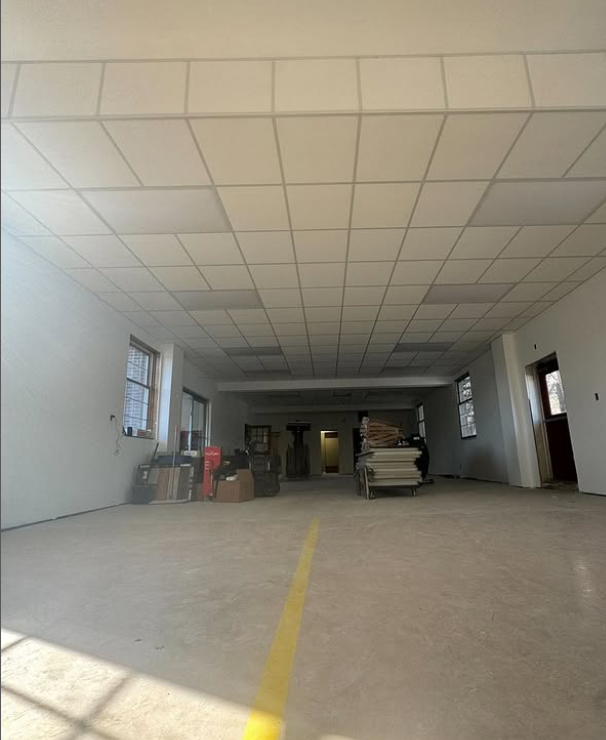 Empty room under construction with white walls, drop ceiling, and concrete floor.