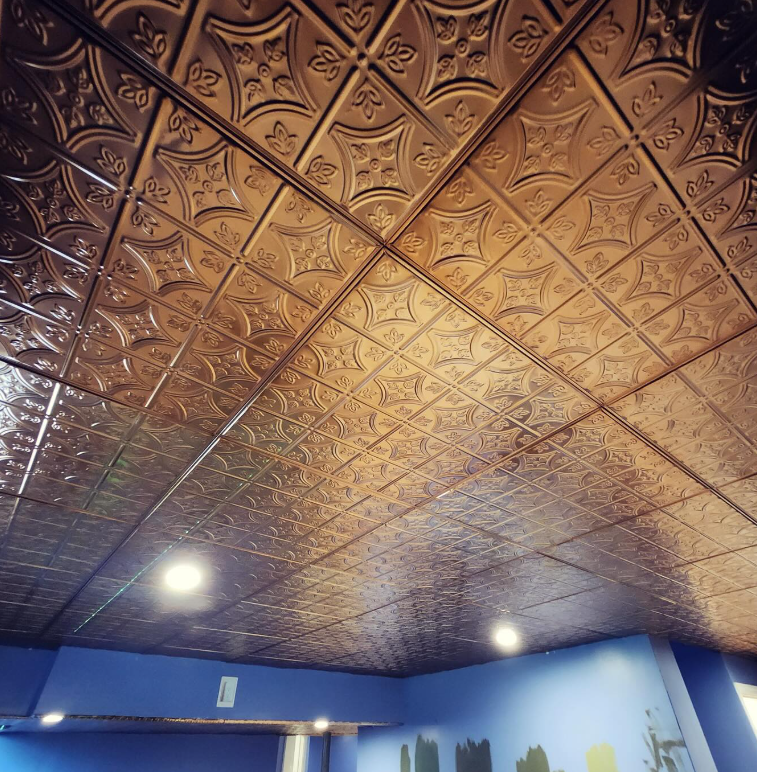 A copper-colored decorative ceiling with a repeating floral pattern above a blue-painted room.