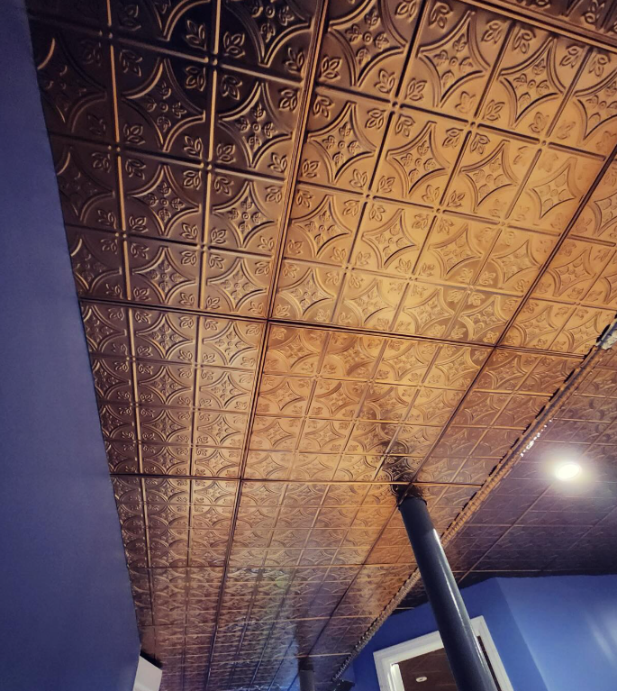 Bronze-toned, patterned ceiling tiles; supporting pillar; blue walls; recessed lighting.