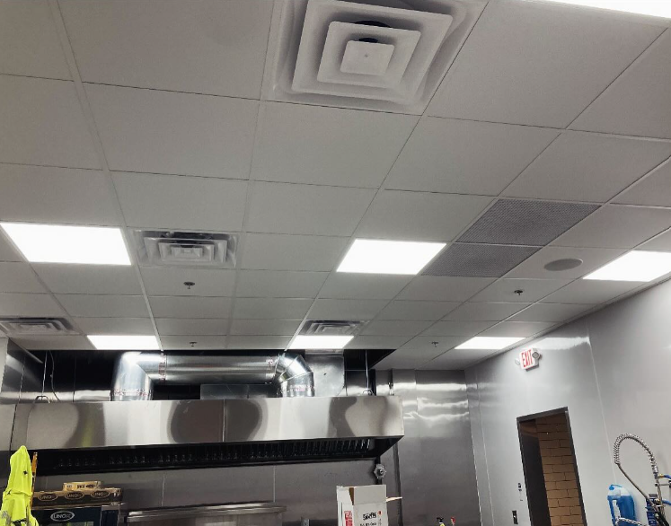 Ceiling of a commercial kitchen with vents, lights, and stainless steel hood.