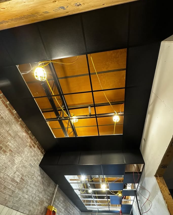 Ceiling under construction with a rectangular opening, exposed beams, and hanging work lights.