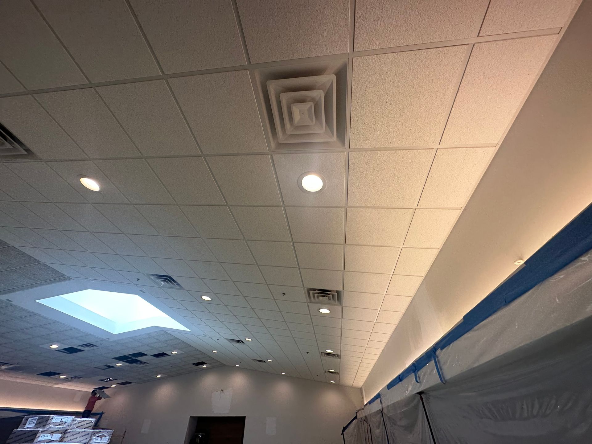 Ceiling tiles with recessed lighting, air vents, and a skylight in a commercial space.
