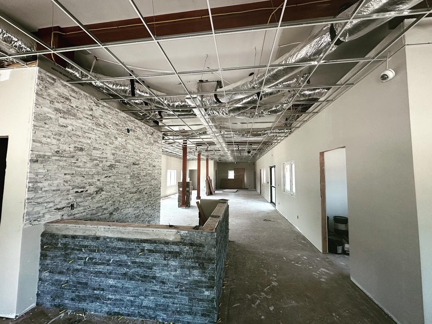 Interior space under construction; exposed ceiling with ductwork; stone and painted walls; unfinished floor.