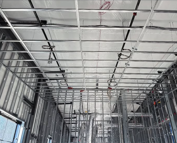 Interior view of a building under construction, showing metal framework for walls and ceiling, with wiring.
