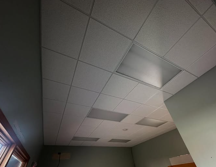 Ceiling with white tiles and recessed fluorescent lights in a room.