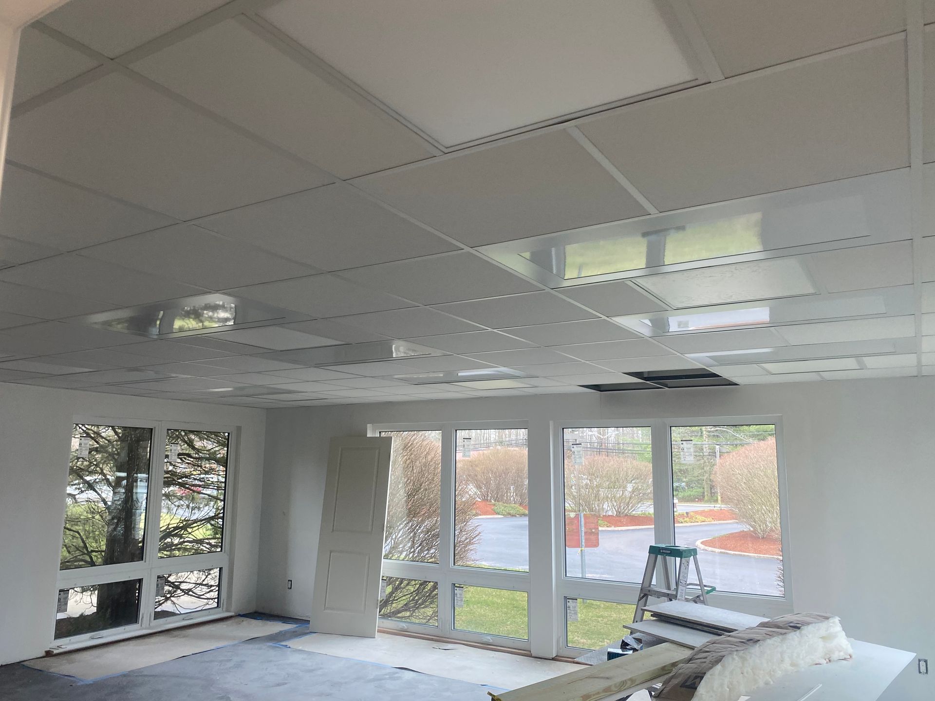 Interior view of a room with a suspended ceiling under construction, large windows, and unfinished walls.