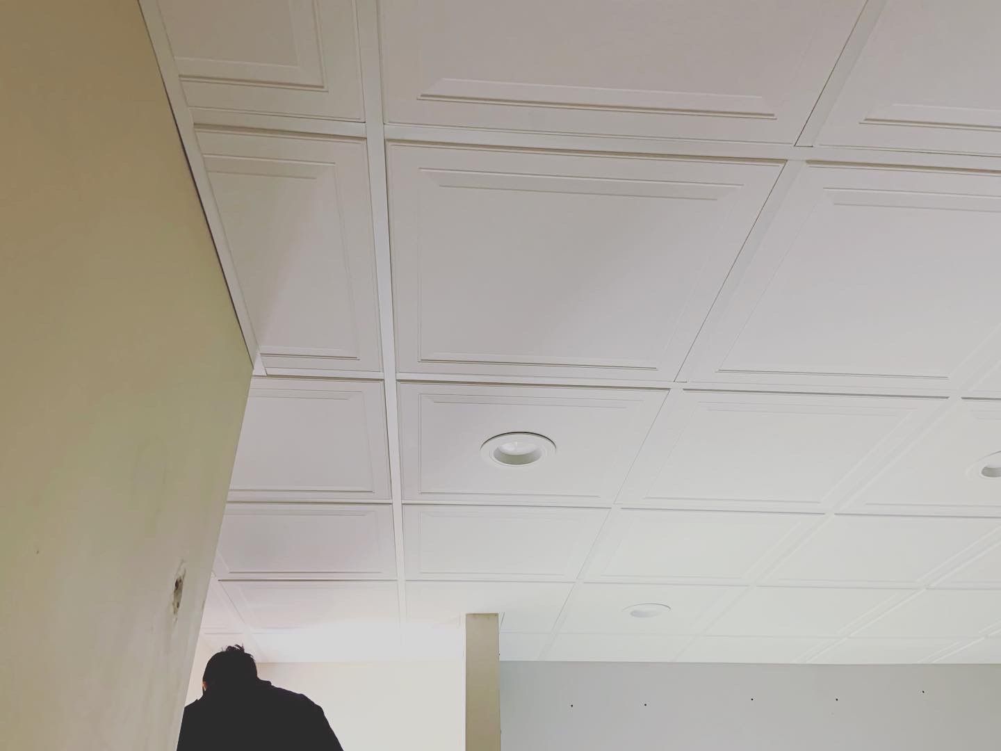 Person walking in a room with a white drop ceiling and beige walls.