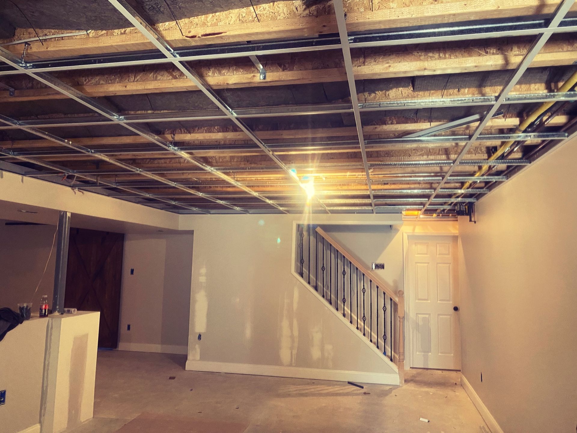 Basement renovation in progress; exposed ceiling beams, unfinished drywall, stairs, and doorway.