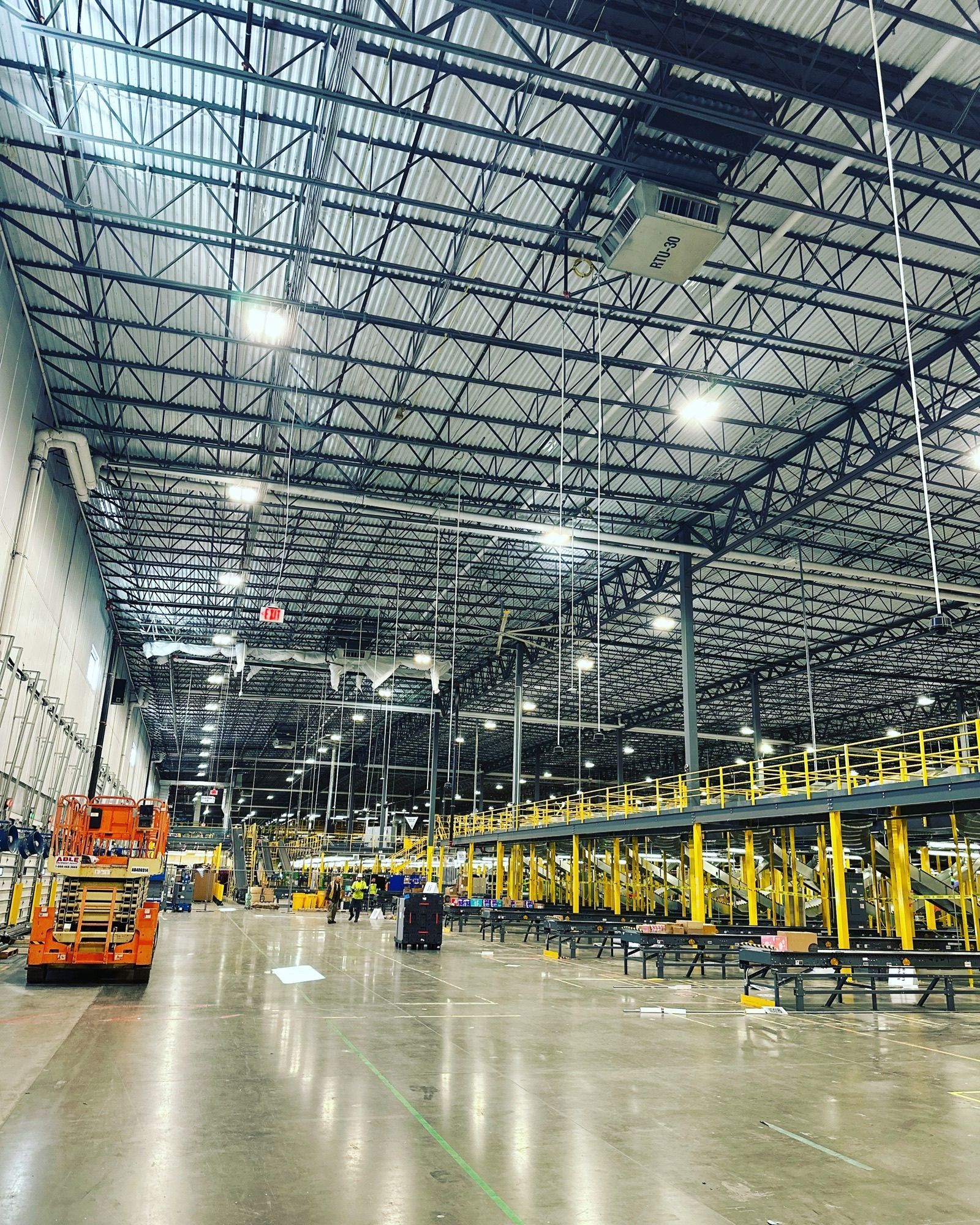Inside a large industrial warehouse: metal beams, high ceilings, machinery, and workers.