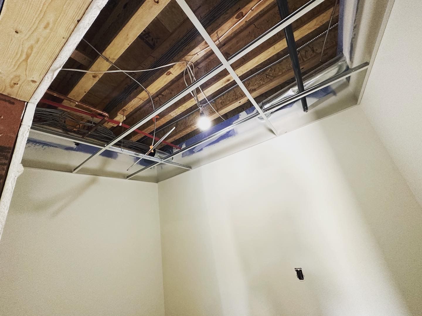 Room with exposed ceiling showing ceiling supports and a hanging light fixture. Walls are painted off-white.