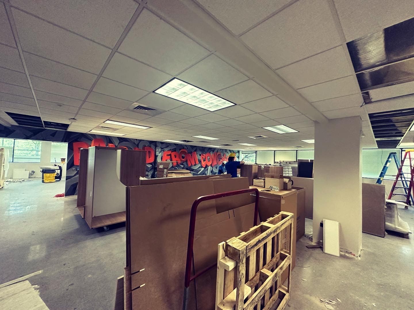 An interior office space under construction, with boxes, equipment, and a person working.