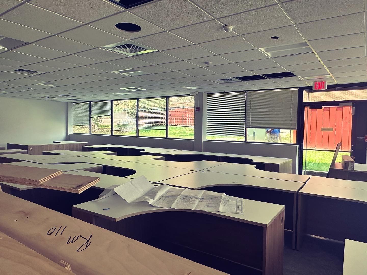 Empty classroom with desks, windows, and an exit door.