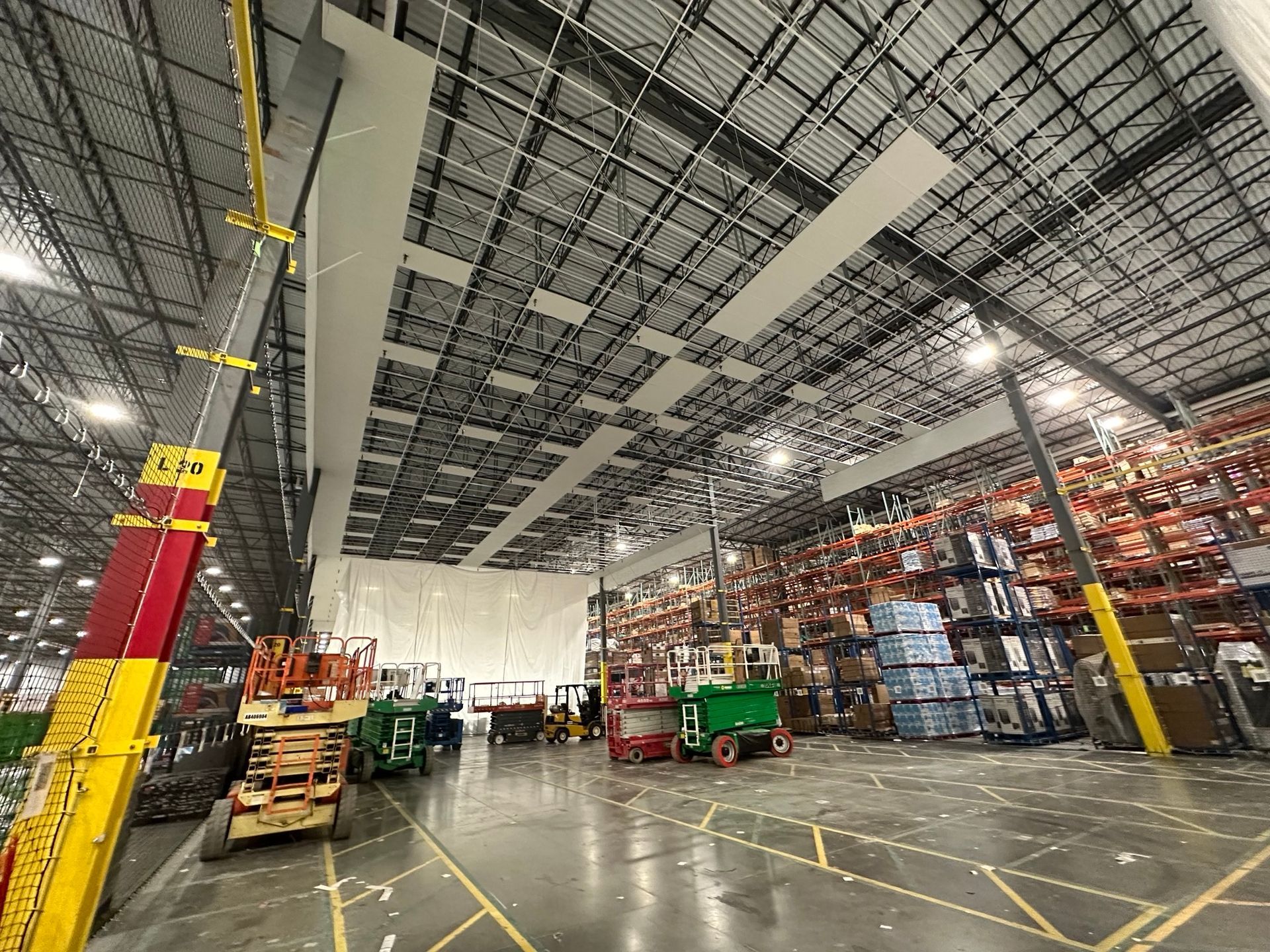 Warehouse interior with forklifts, inventory racks, and a lift extending towards the ceiling.