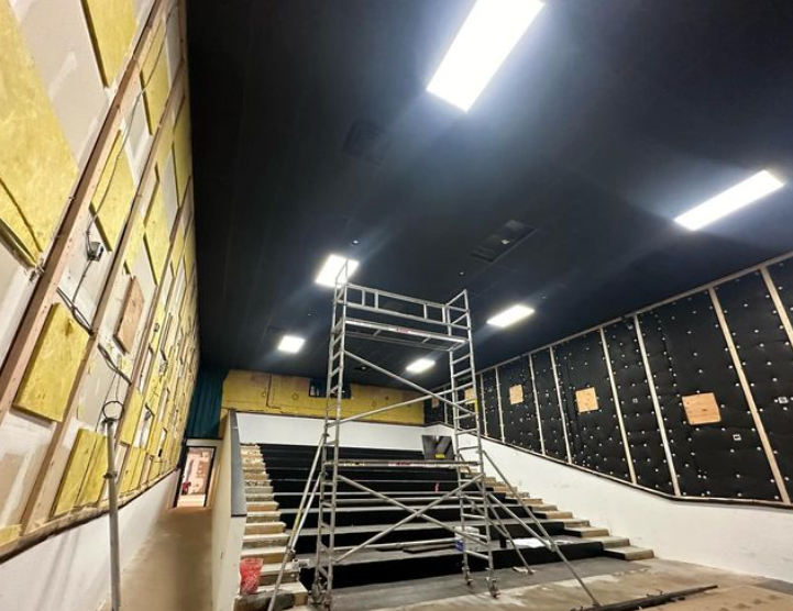 Construction site. Interior view of a theater-like space with a scaffolding, stairs, and exposed insulation. 