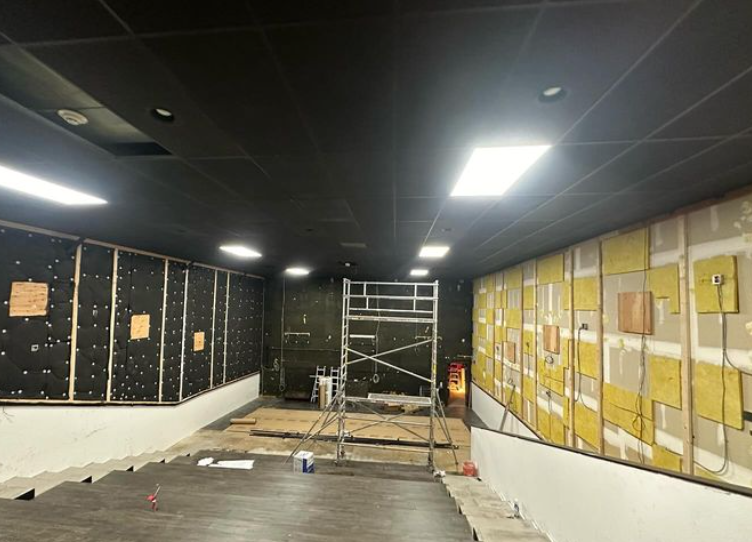Interior under construction; walls and ceiling painted black, exposed insulation, scaffolding, and recessed lighting.