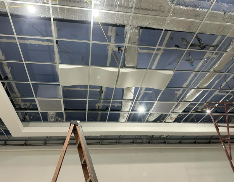 Damaged drop ceiling with metal grid, insulation, and exposed structure. A ladder leans against the wall.