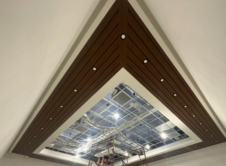 Triangular wooden ceiling with recessed lights, surrounding a glass skylight with scaffolding.